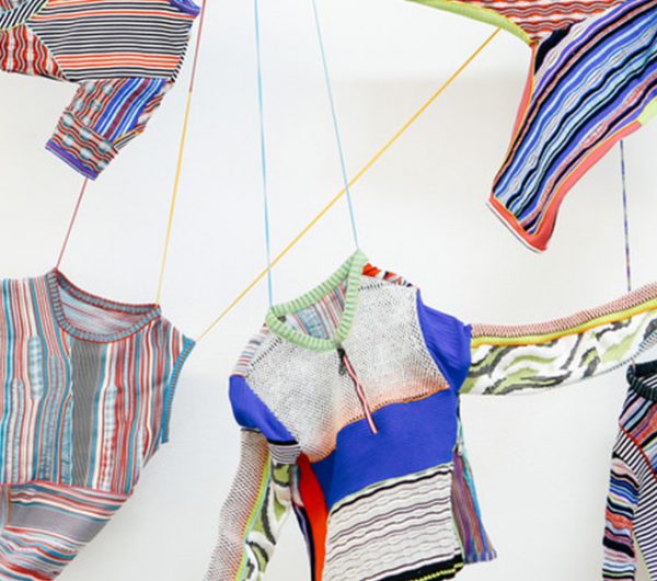Collection of knitted garments hung off the wall with various yarns