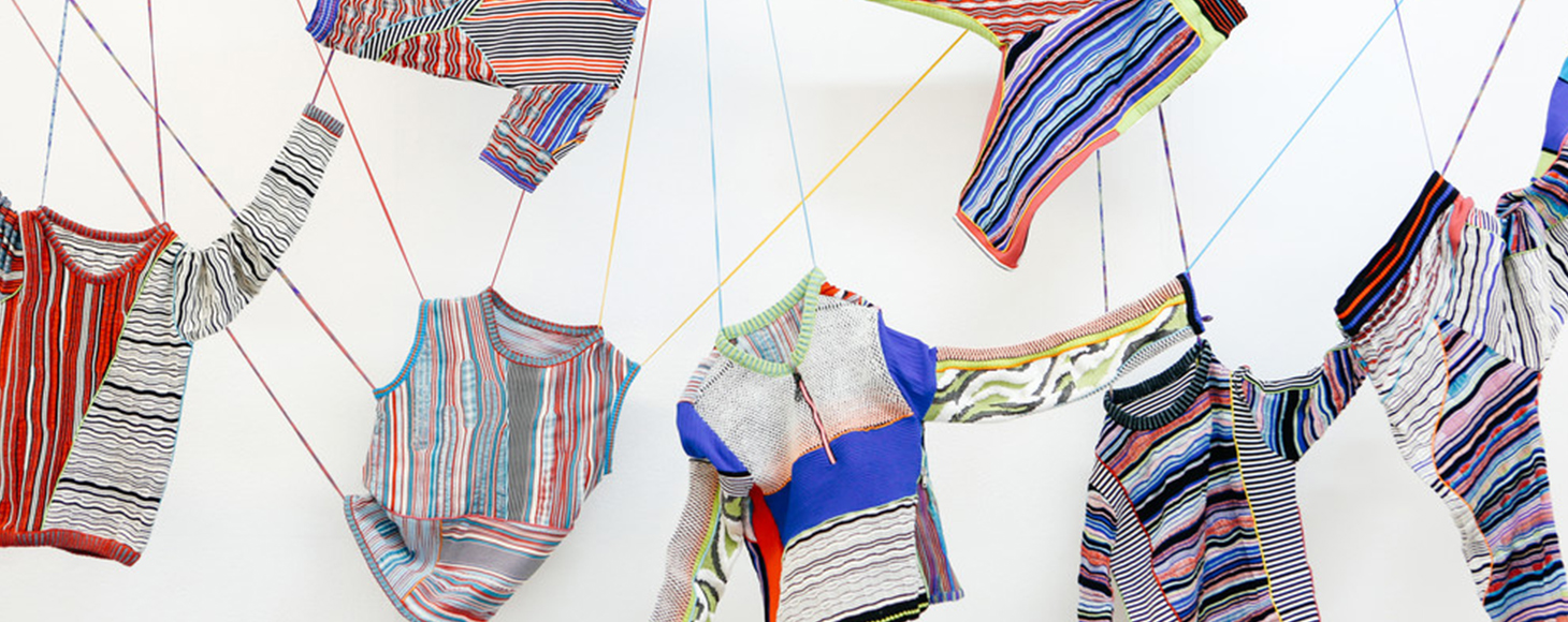 Collection of knitted garments hung off the wall with various yarns