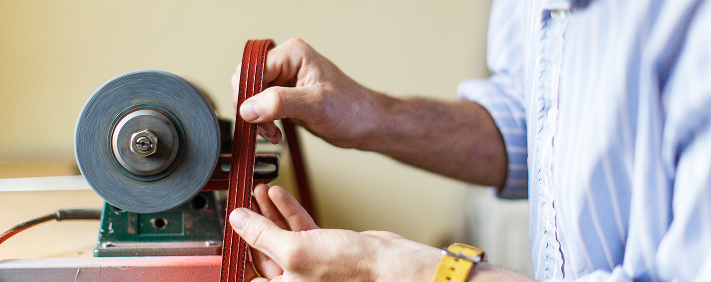 A man is working in his workshop smoothing the edges of fire hose pipe product which will be used to make bags and belts
